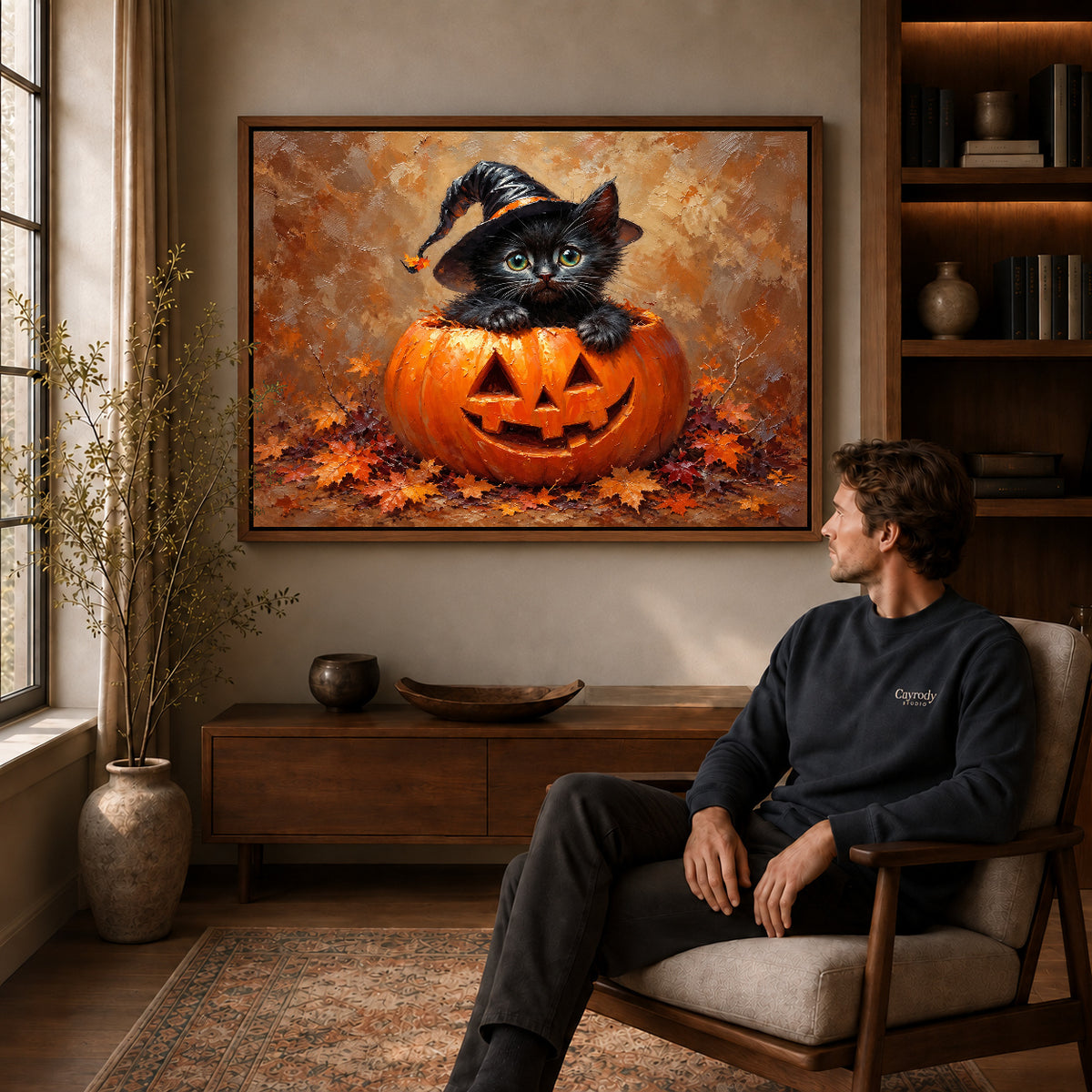 Pumpkin kitten canvas art in a walnut frame above a console beside a seated man.