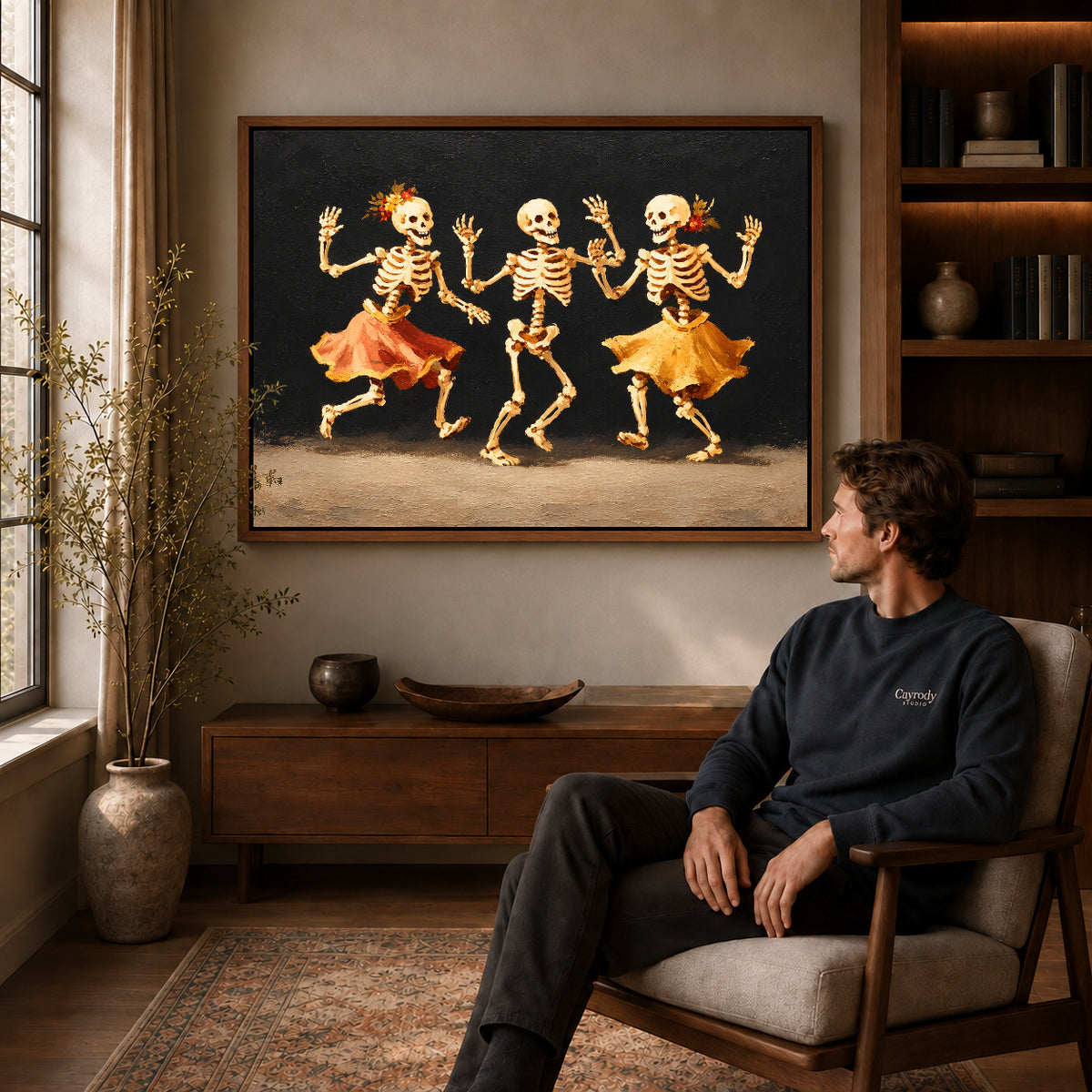 Dancing Skeletons canvas art in a walnut frame above a console beside a seated man.