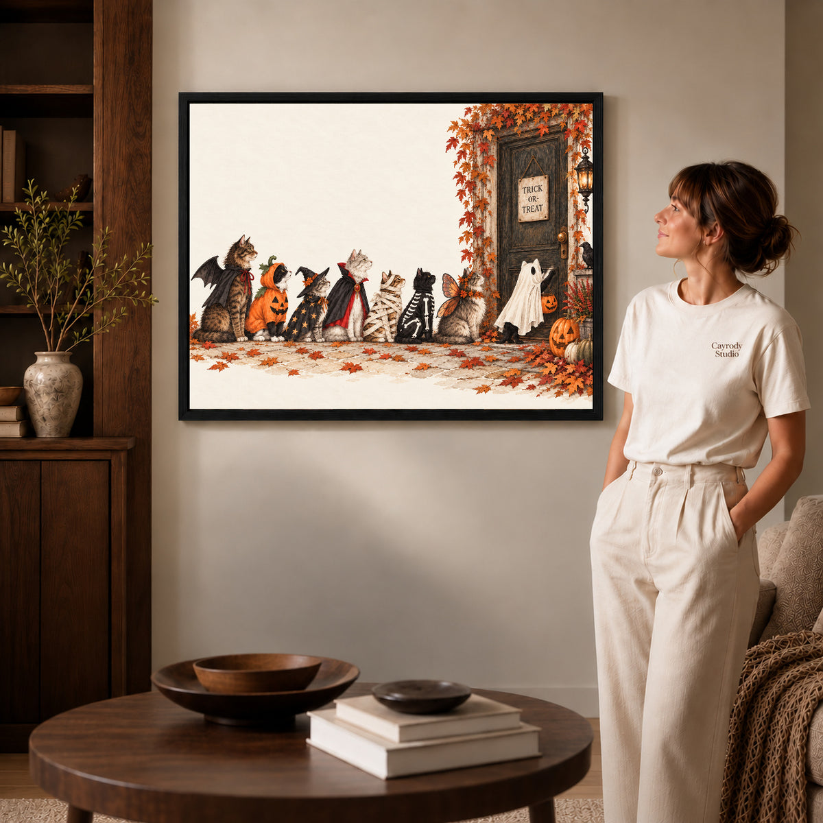 Halloween cat canvas art in a black frame above a round table beside a standing woman.