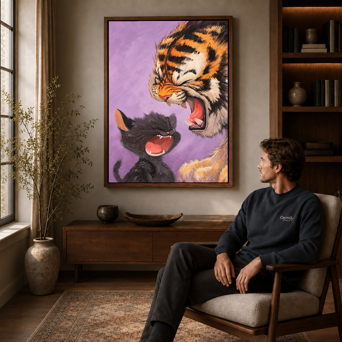 Laughing Tiger Kitten canvas art in a walnut frame above a console beside a seated man.
