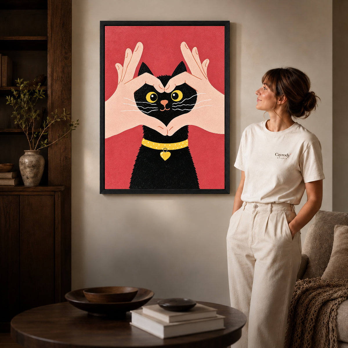 Heart kitten canvas art in a black frame beside a woman and round wooden table.