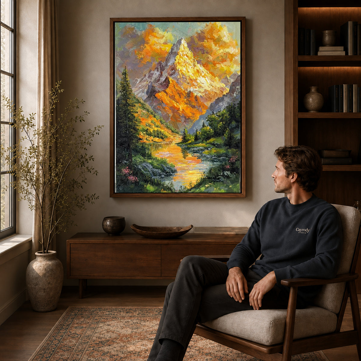 Alpine lake canvas art in a walnut frame above a console beside a seated man.