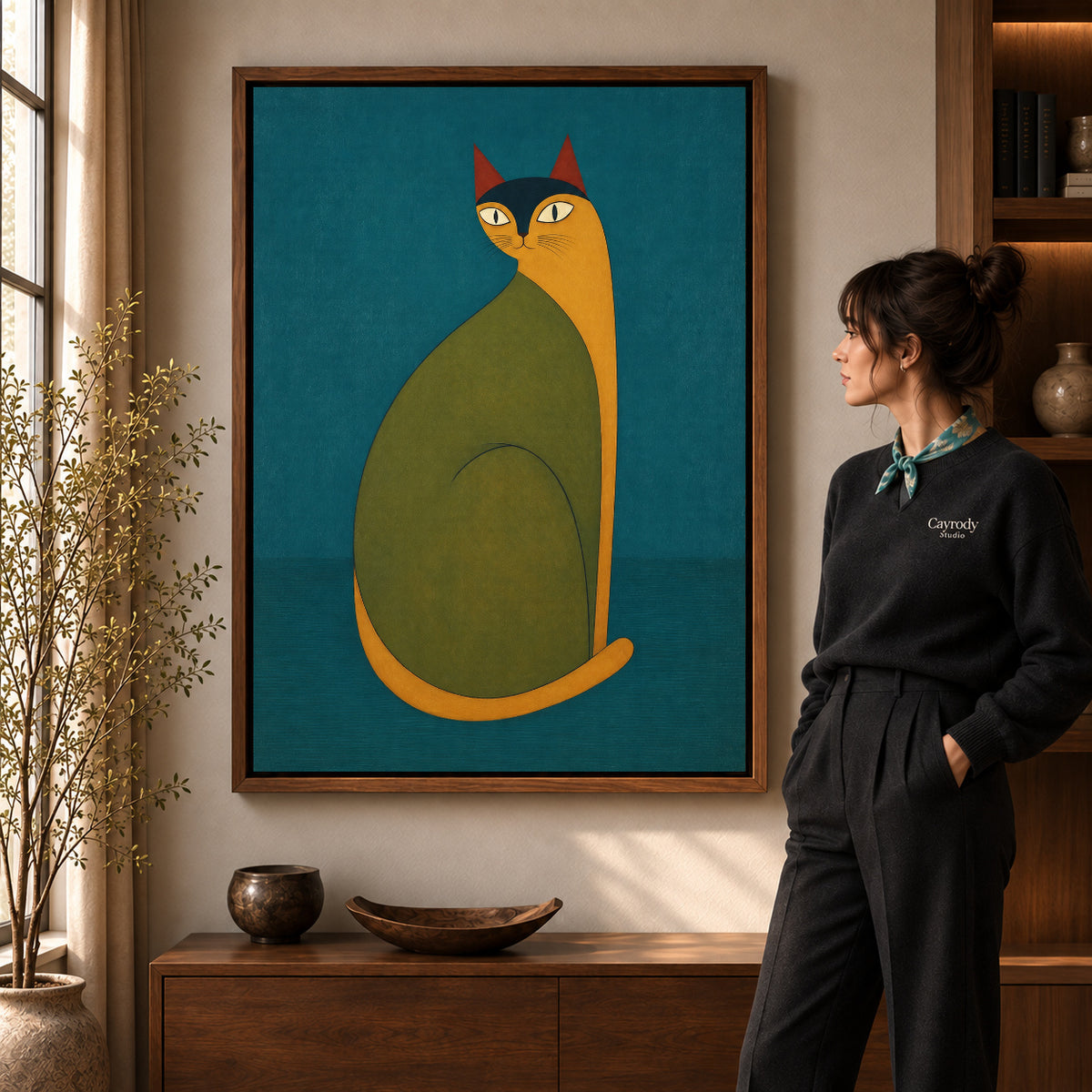 Folk cat canvas art in a walnut frame beside a standing woman and wooden console.