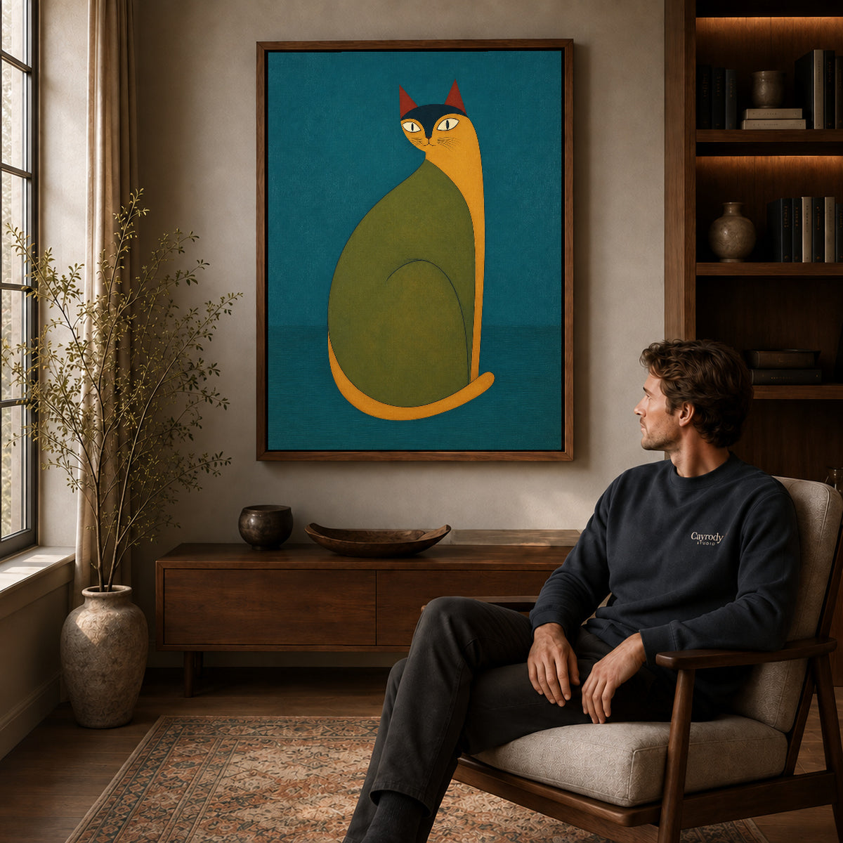 Folk cat canvas art in a walnut frame above a console beside a seated man.