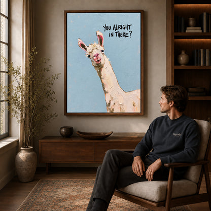 Curious llama canvas art in a walnut frame above a console beside a seated man.