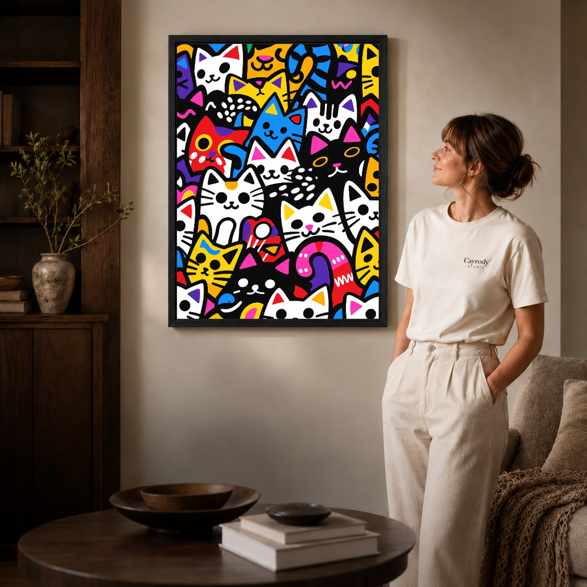 Colorful Cat Collage canvas art in a black frame beside a woman and round wooden table.
