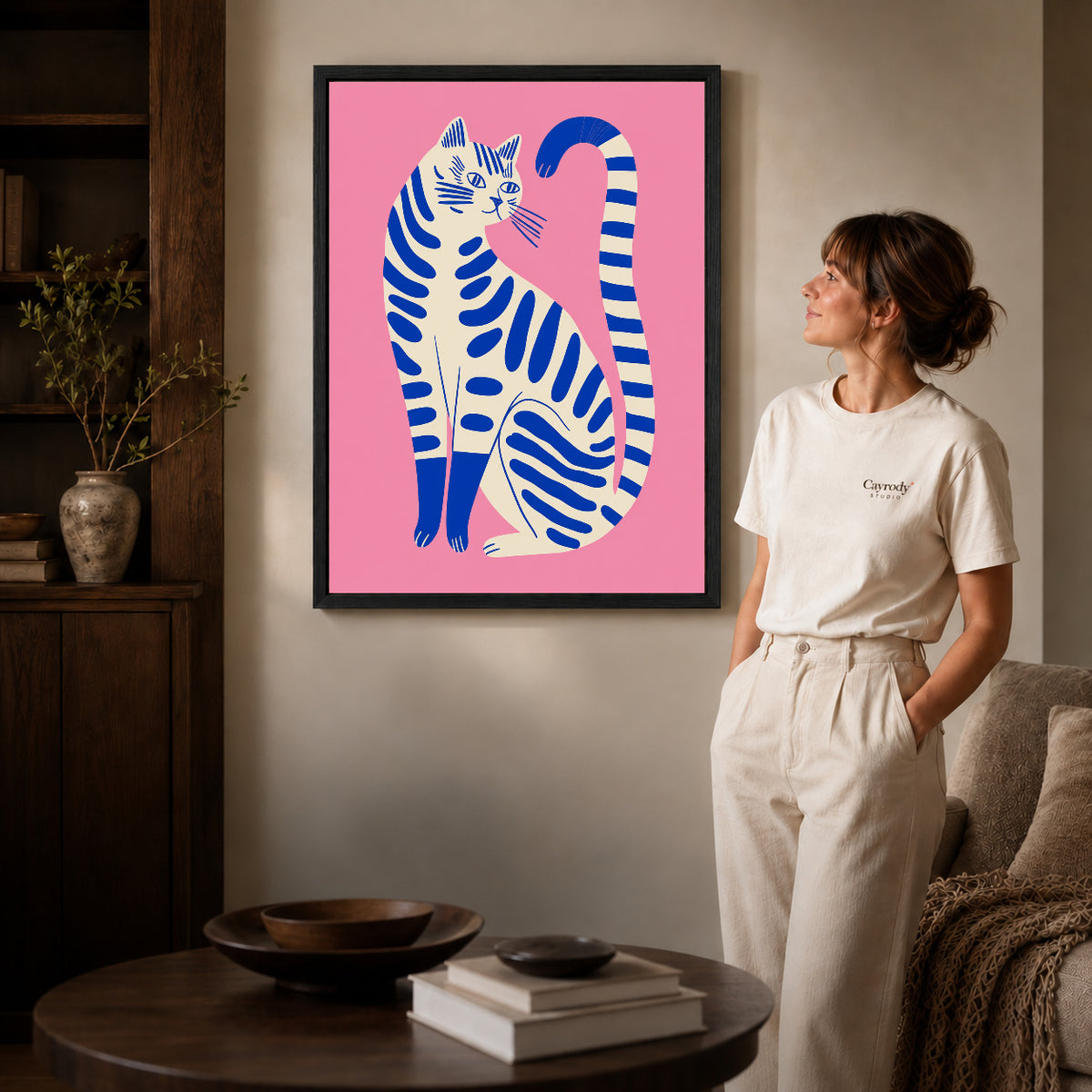 Striped cat canvas art in a black frame beside a woman and round wooden table.