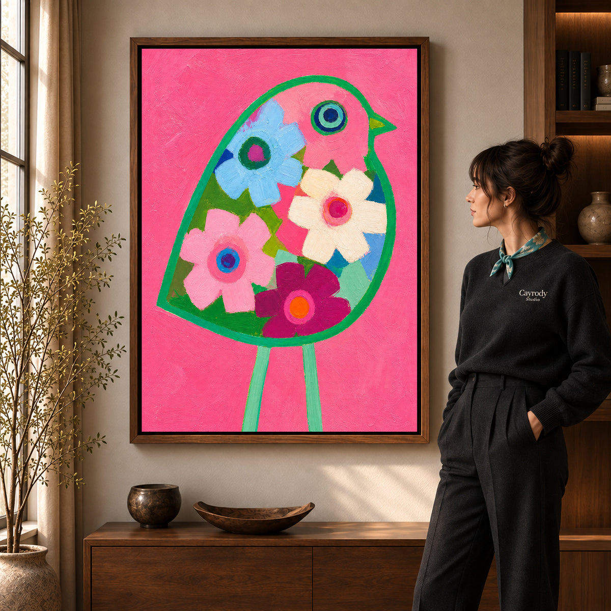 Floral bird canvas art in a walnut frame beside a standing woman and wooden console.