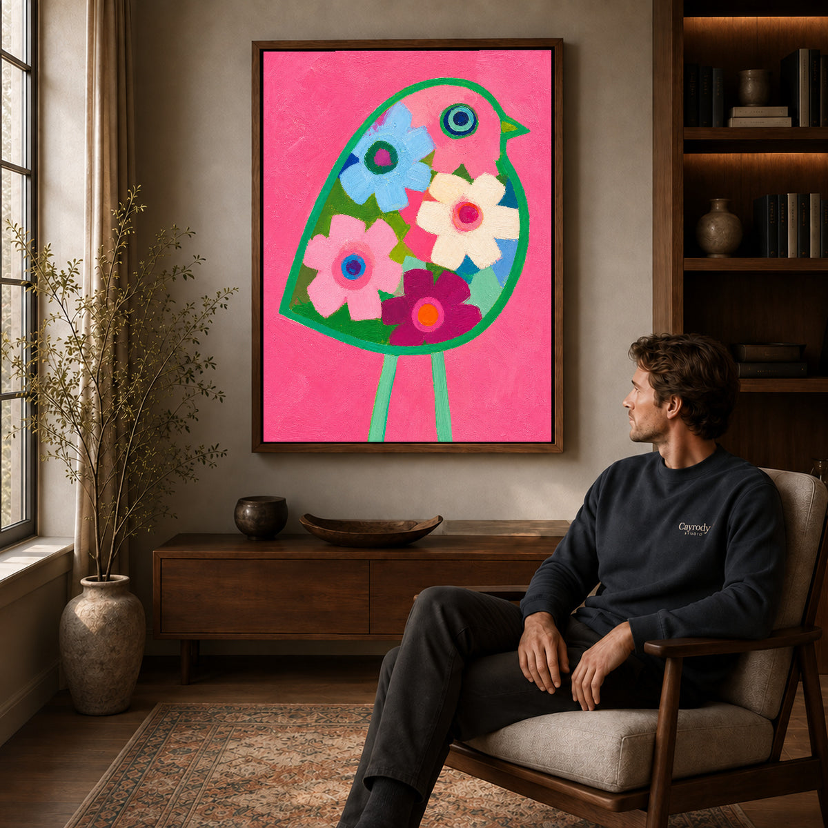 Floral bird canvas art in a walnut frame above a console beside a seated man.