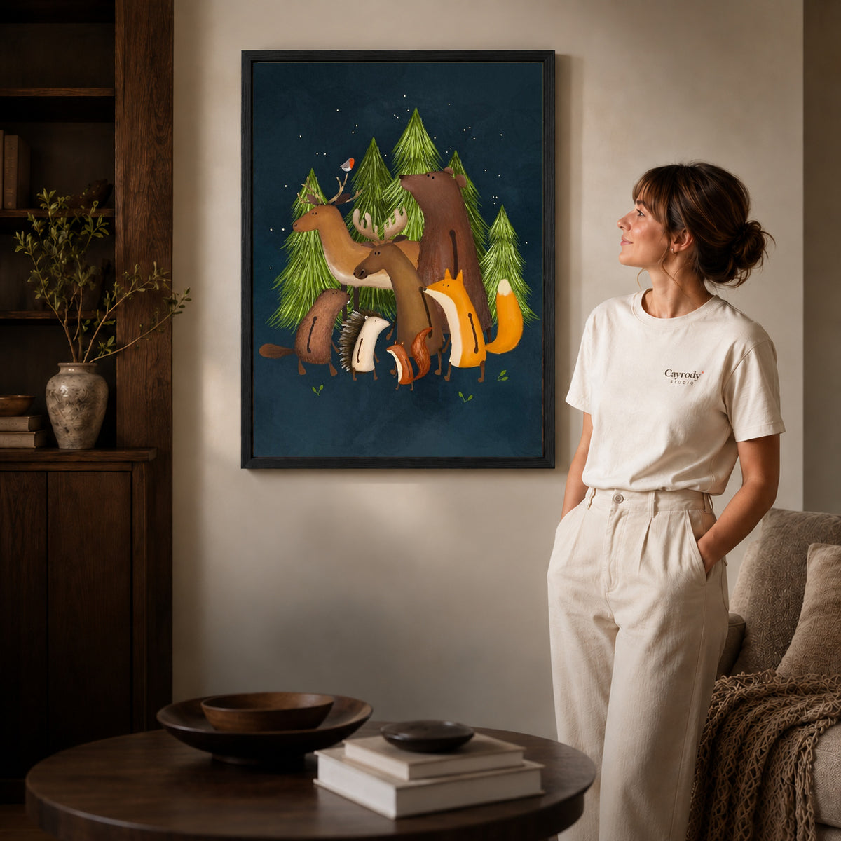 Woodland friends canvas art in a black frame beside a woman and round wooden table.