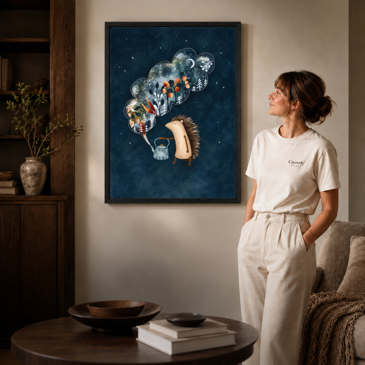 Hedgehog canvas art in a black frame beside a woman and round wooden table.