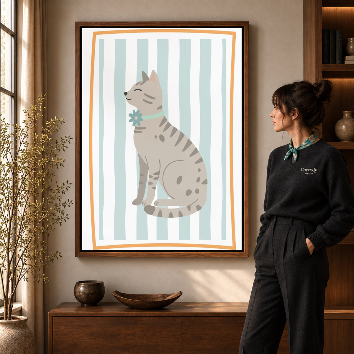 Tabby cat canvas art in a walnut frame beside a standing woman and wooden console.