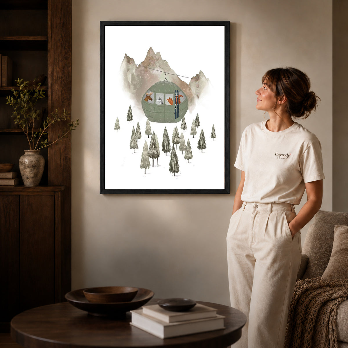 Ski gondola canvas art in a black frame beside a woman and round wooden table.