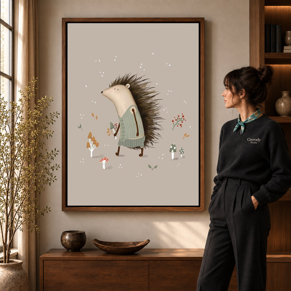 Hedgehog sweater canvas art in a walnut frame beside a standing woman and wooden console.