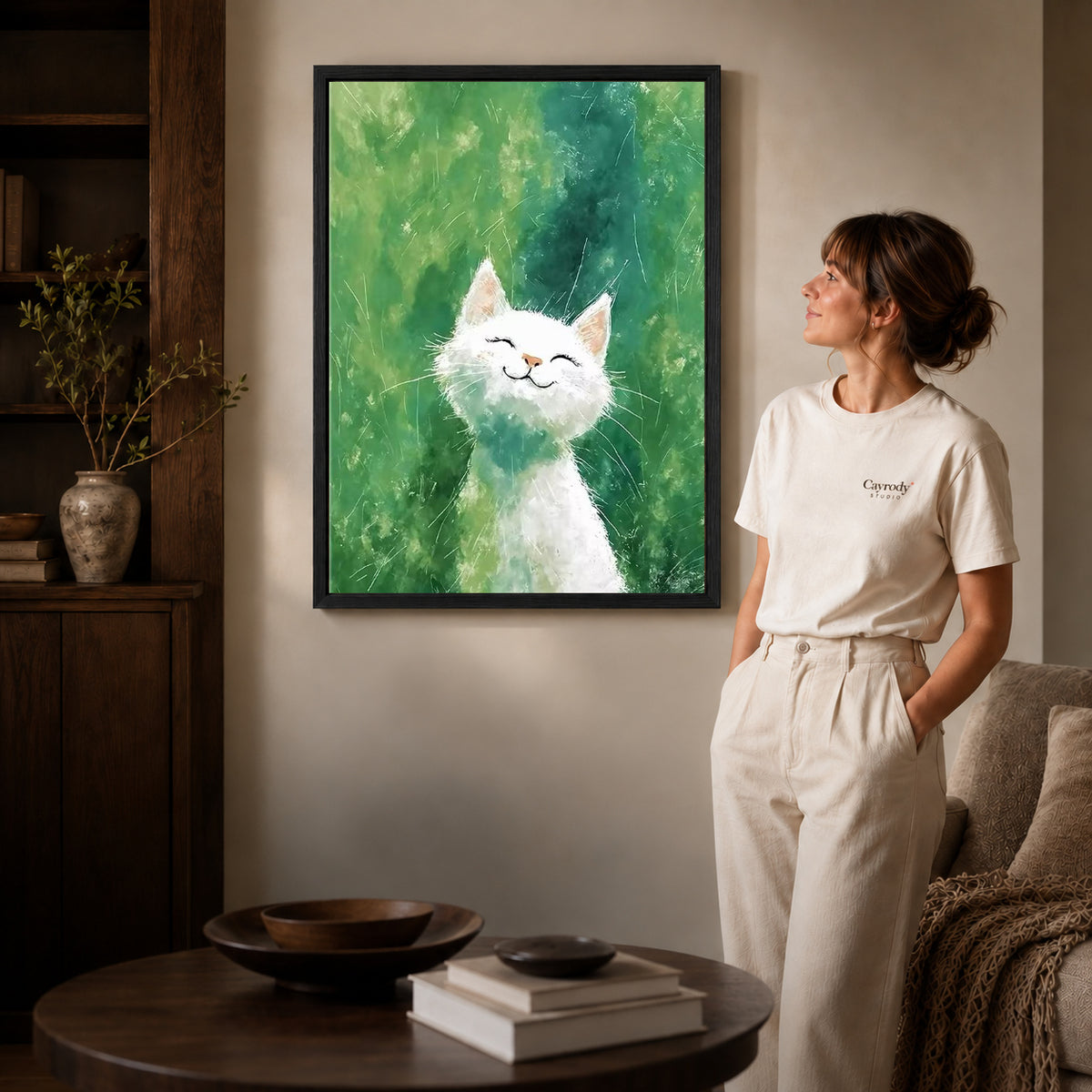 White cat canvas art in a black frame beside a woman and round wooden table.