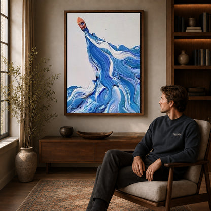 Blue wave canvas art in a walnut frame above a console beside a seated man.