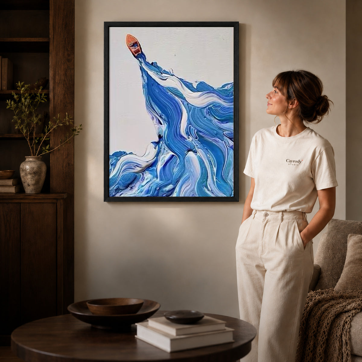 Blue wave canvas art in a black frame beside a woman and round wooden table.
