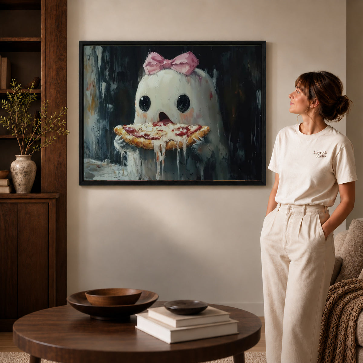 Pizza ghost canvas art in a black frame beside a woman and round wooden table.