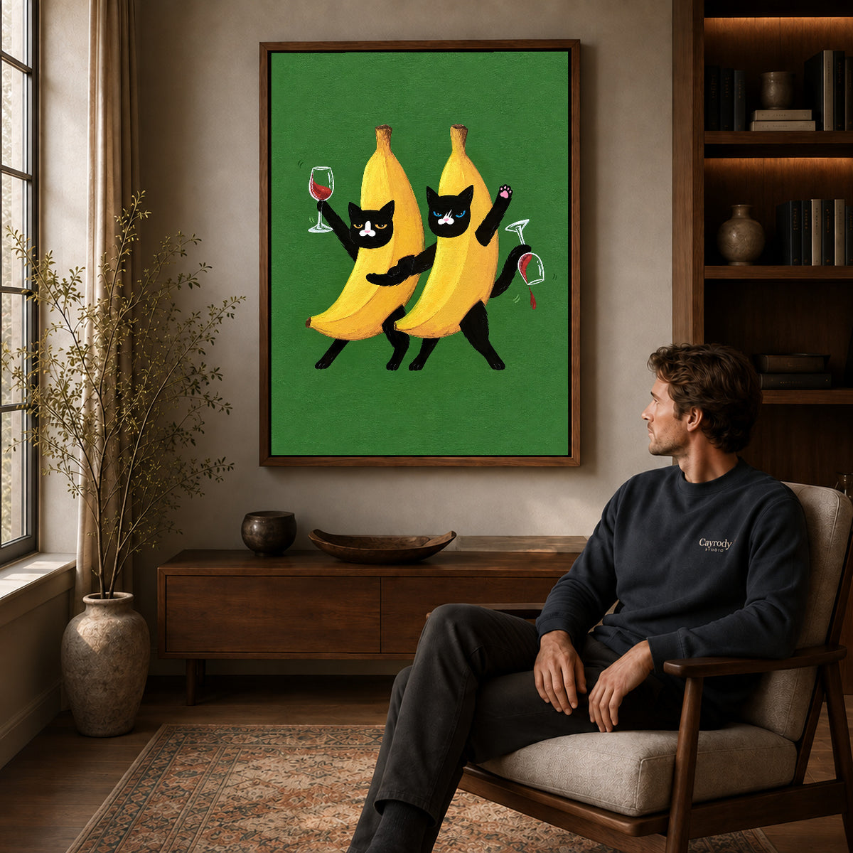 Banana cats canvas art in a walnut frame above a console beside a seated man.