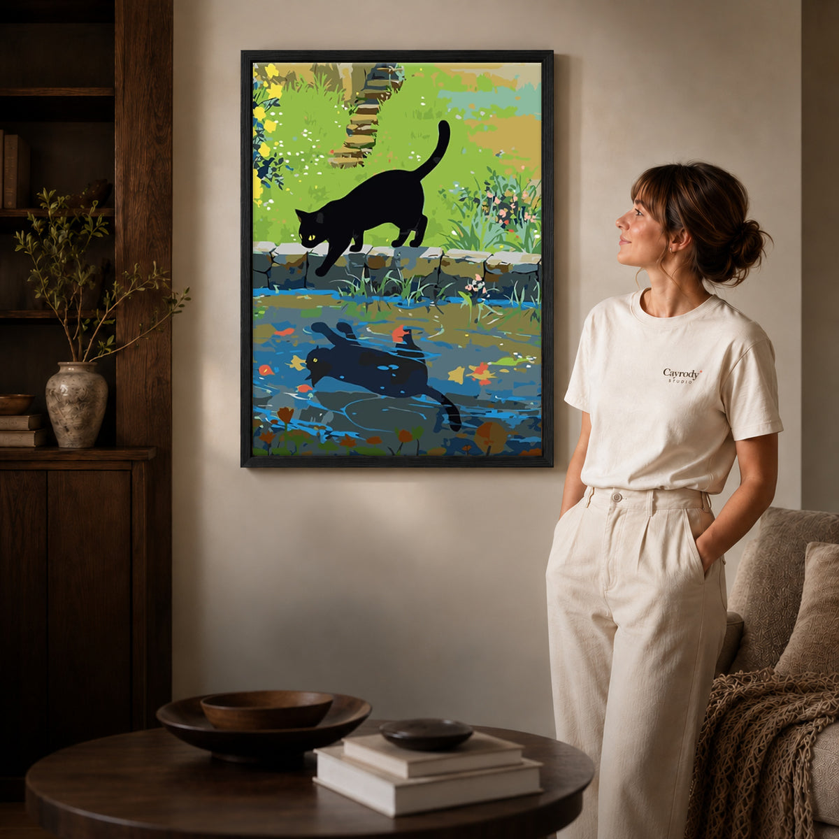 Black cat canvas art in a black frame beside a woman and round wooden table.