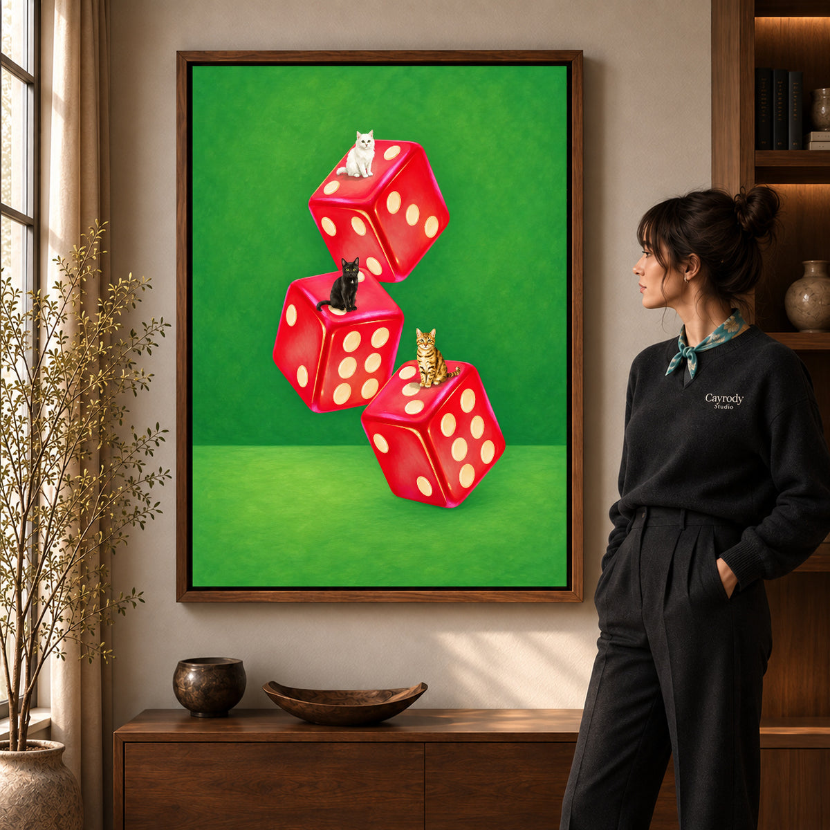 Cats and dice canvas art in a walnut frame beside a standing woman and wooden console.