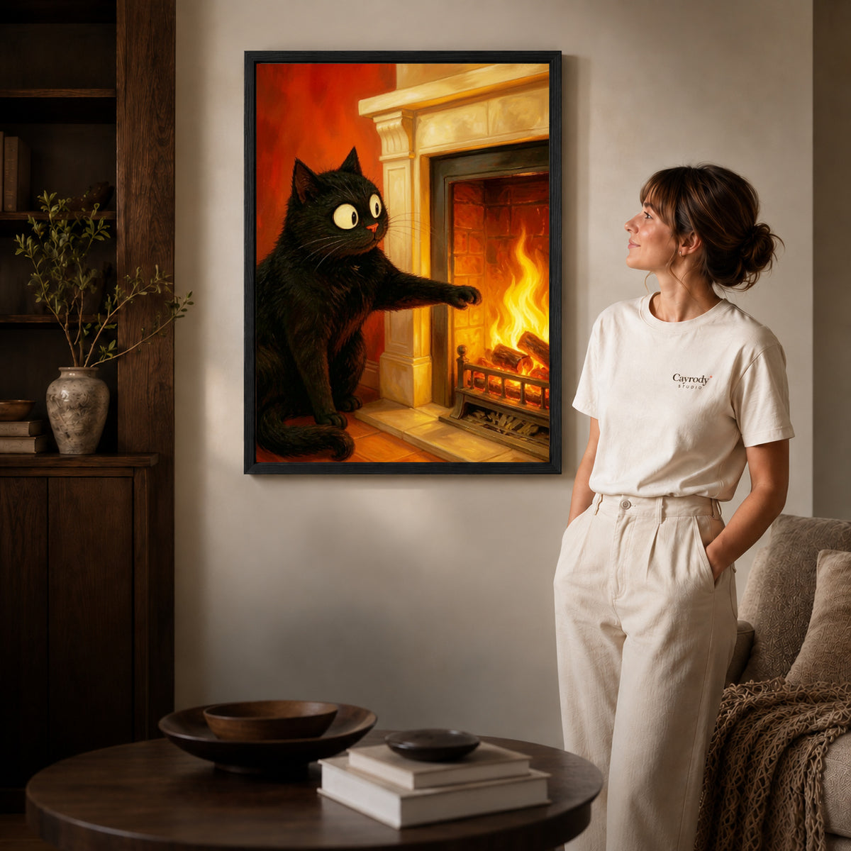 Fireplace cat canvas art in a black frame beside a woman and round wooden table.