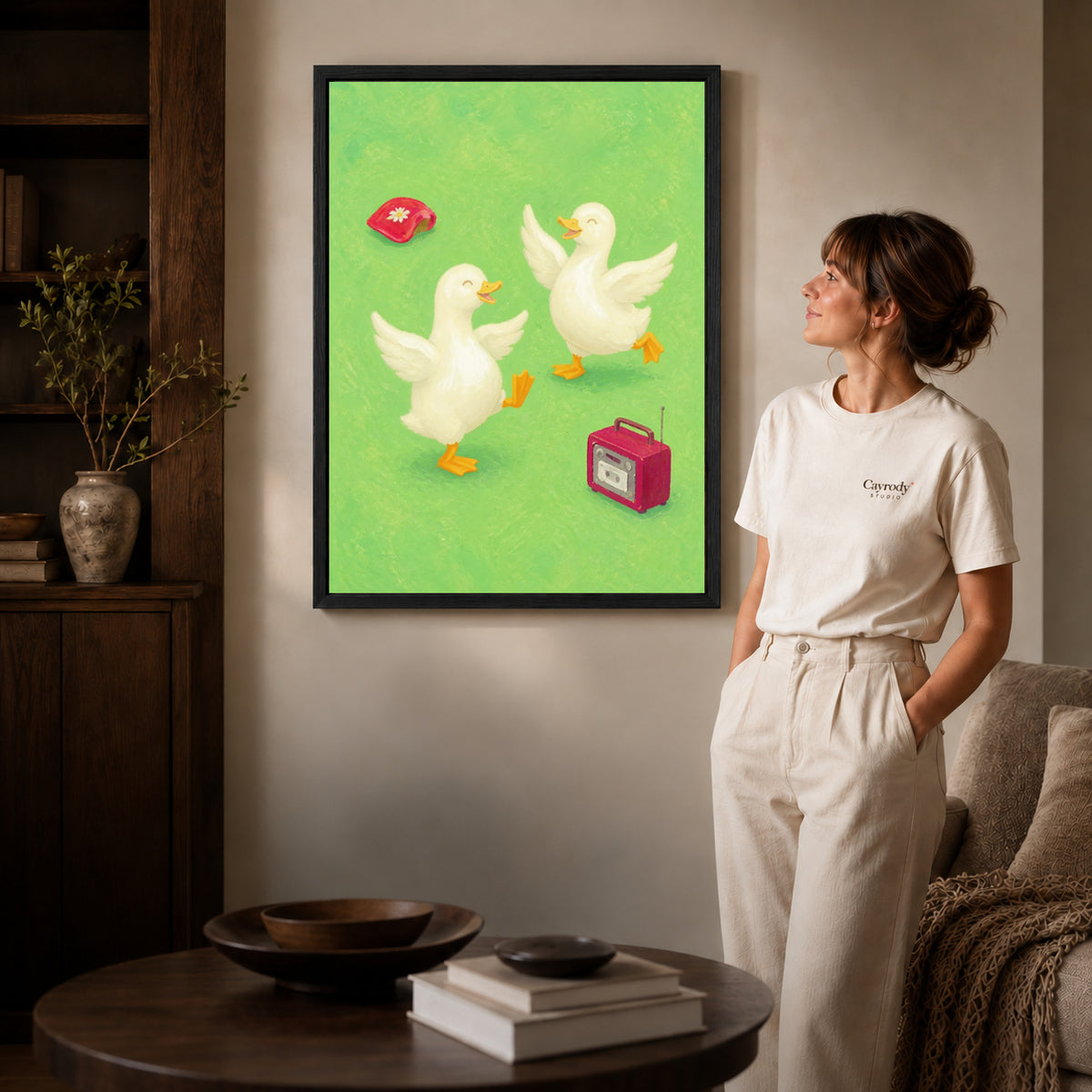 Dancing ducks canvas art in a black frame beside a woman and round wooden table.