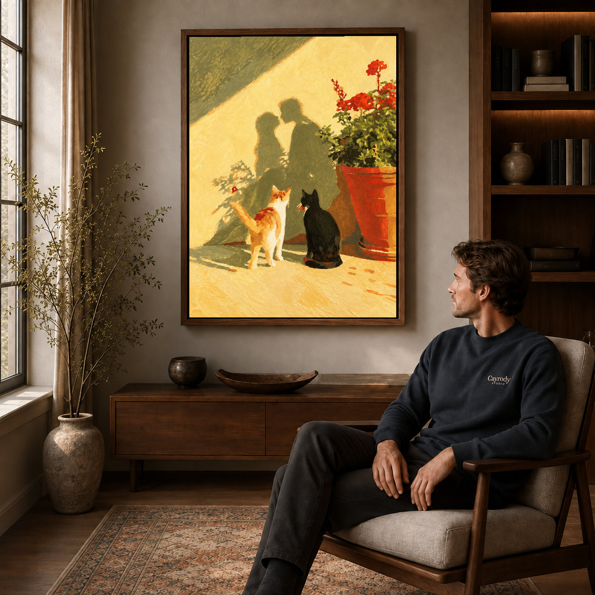 Sunlit cats canvas art in a walnut frame above a console beside a seated man.