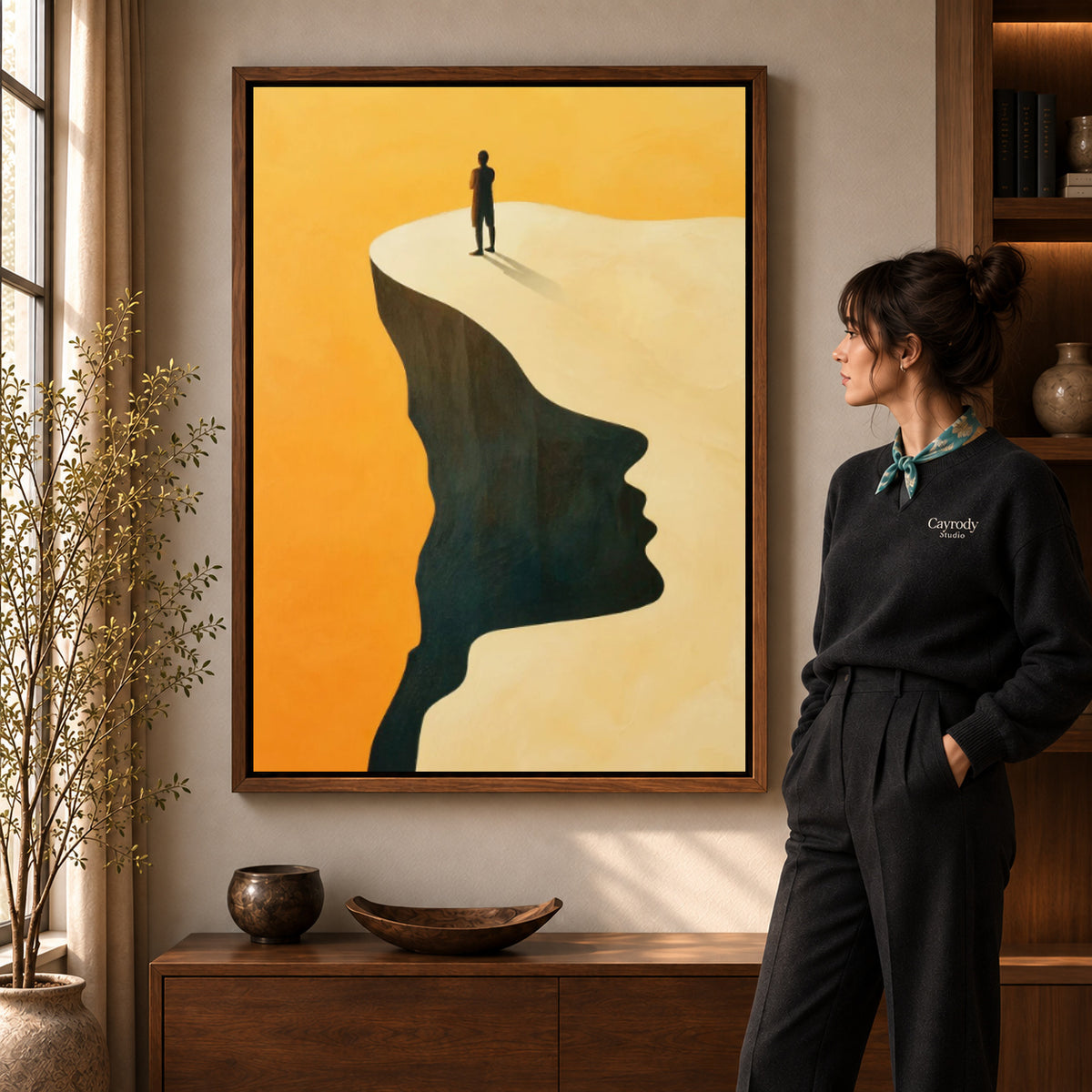 Surreal landscape canvas art in a walnut frame beside a standing woman and wooden console.