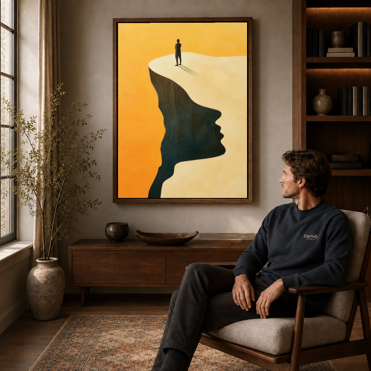 Surreal landscape canvas art in a walnut frame above a console beside a seated man.