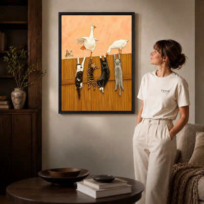 Geese and cats canvas art in a black frame beside a woman and round wooden table.