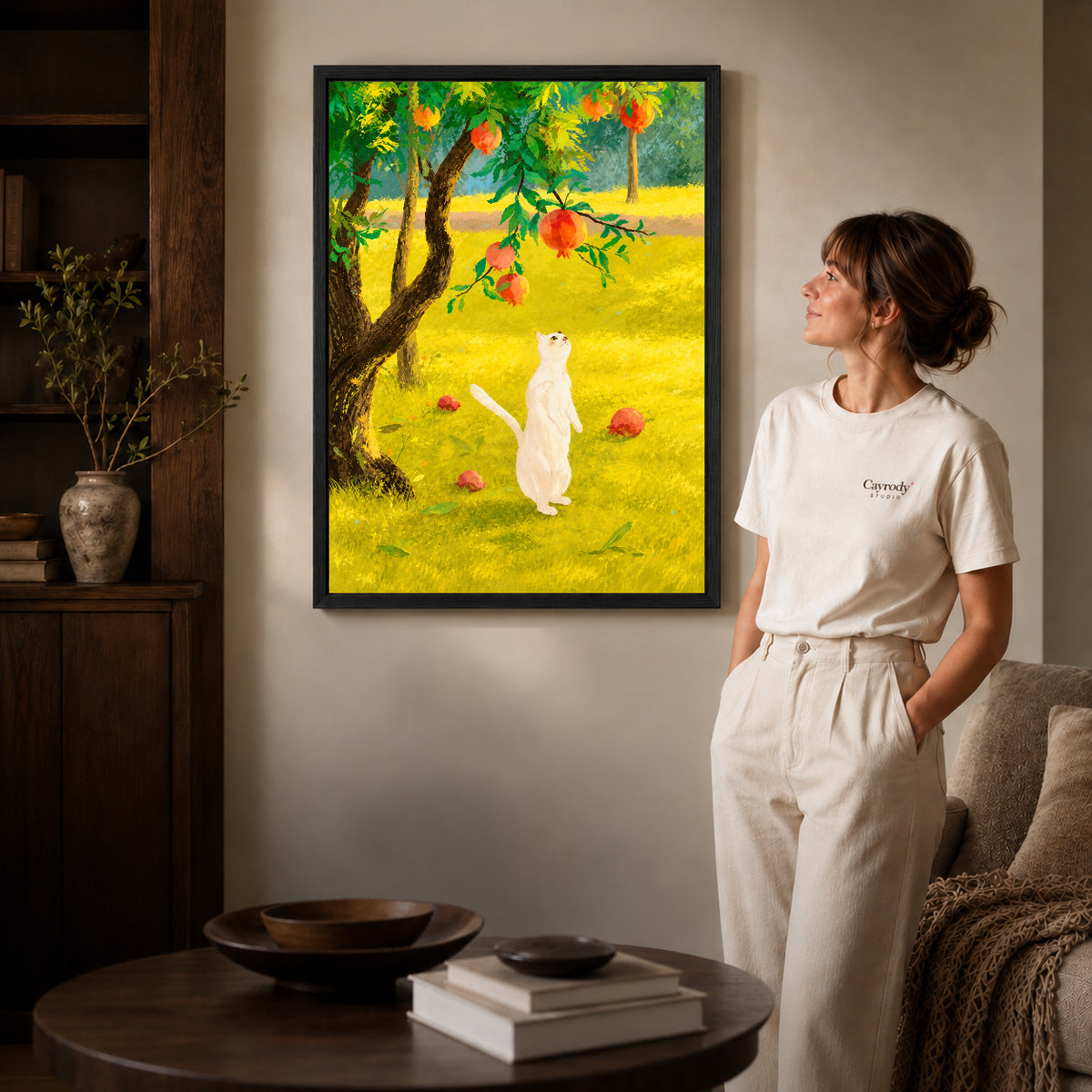 Orchard cat canvas art in a black frame beside a woman and round wooden table.