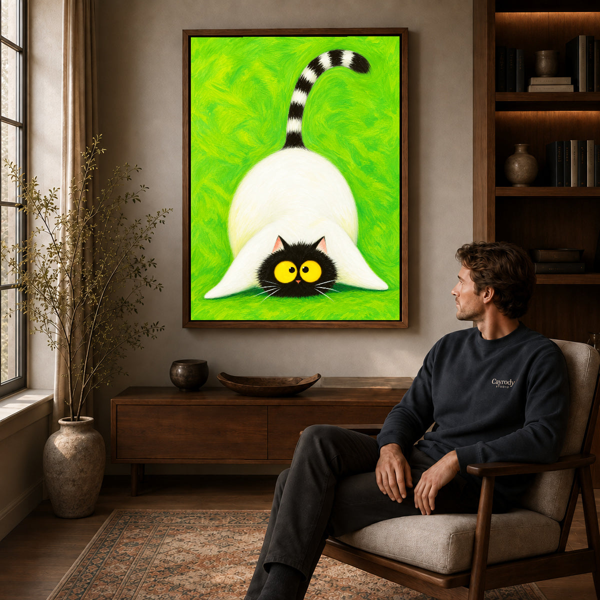 Playful cat canvas art in a walnut frame above a console beside a seated man.