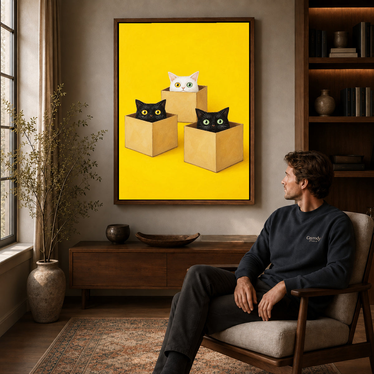 Cats in boxes canvas art in a walnut frame above a console beside a seated man.