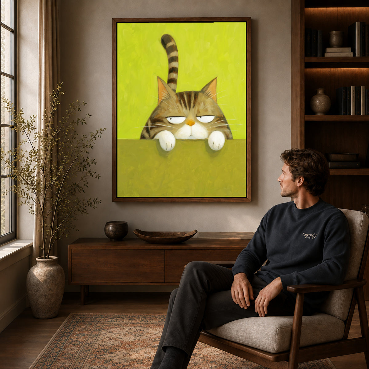 Grumpy tabby canvas art in a walnut frame above a console beside a seated man.