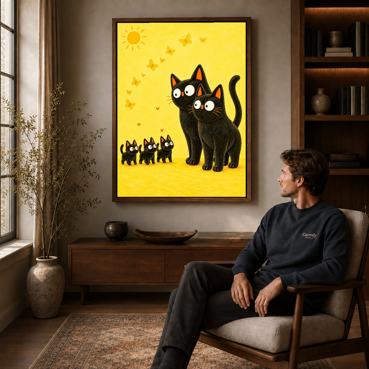 Black cat family canvas art in a walnut frame above a console beside a seated man.