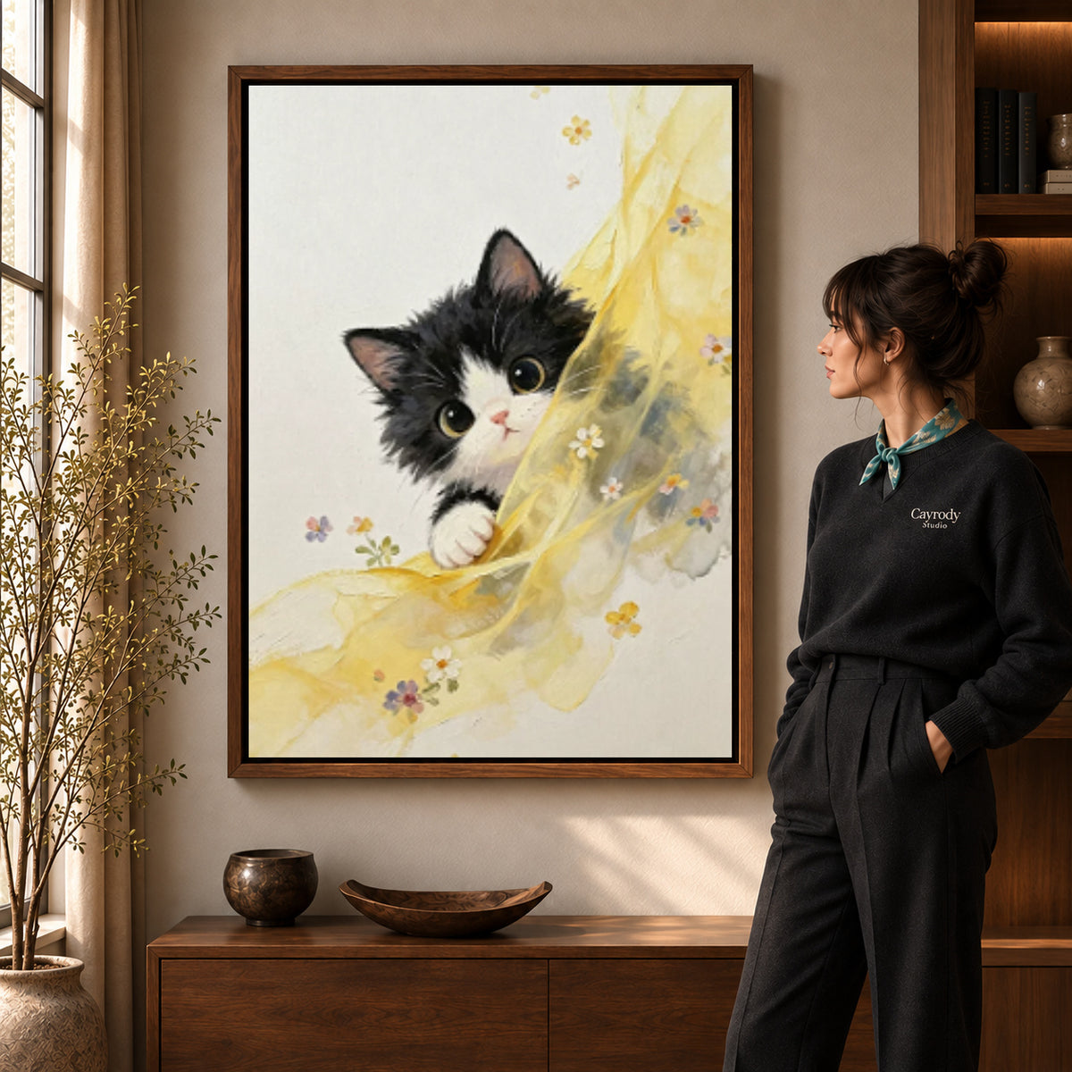 Curious kitten canvas art in a walnut frame beside a standing woman and wooden console.