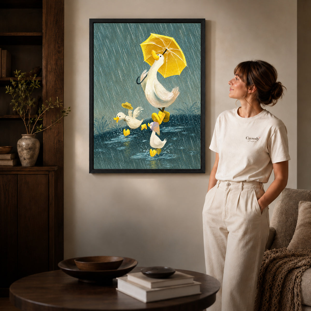 Rainy ducks canvas art in a black frame beside a woman and round wooden table.