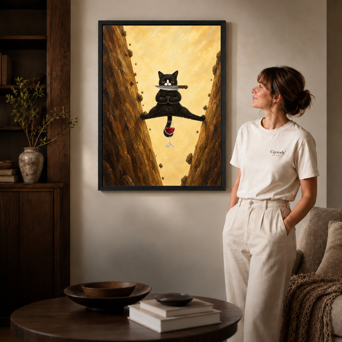 Acrobatic cat canvas art in a black frame beside a woman and round wooden table.