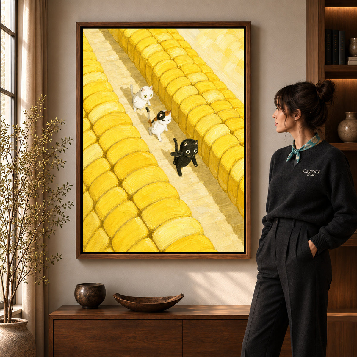 Farm cats canvas art in a walnut frame beside a standing woman and wooden console.
