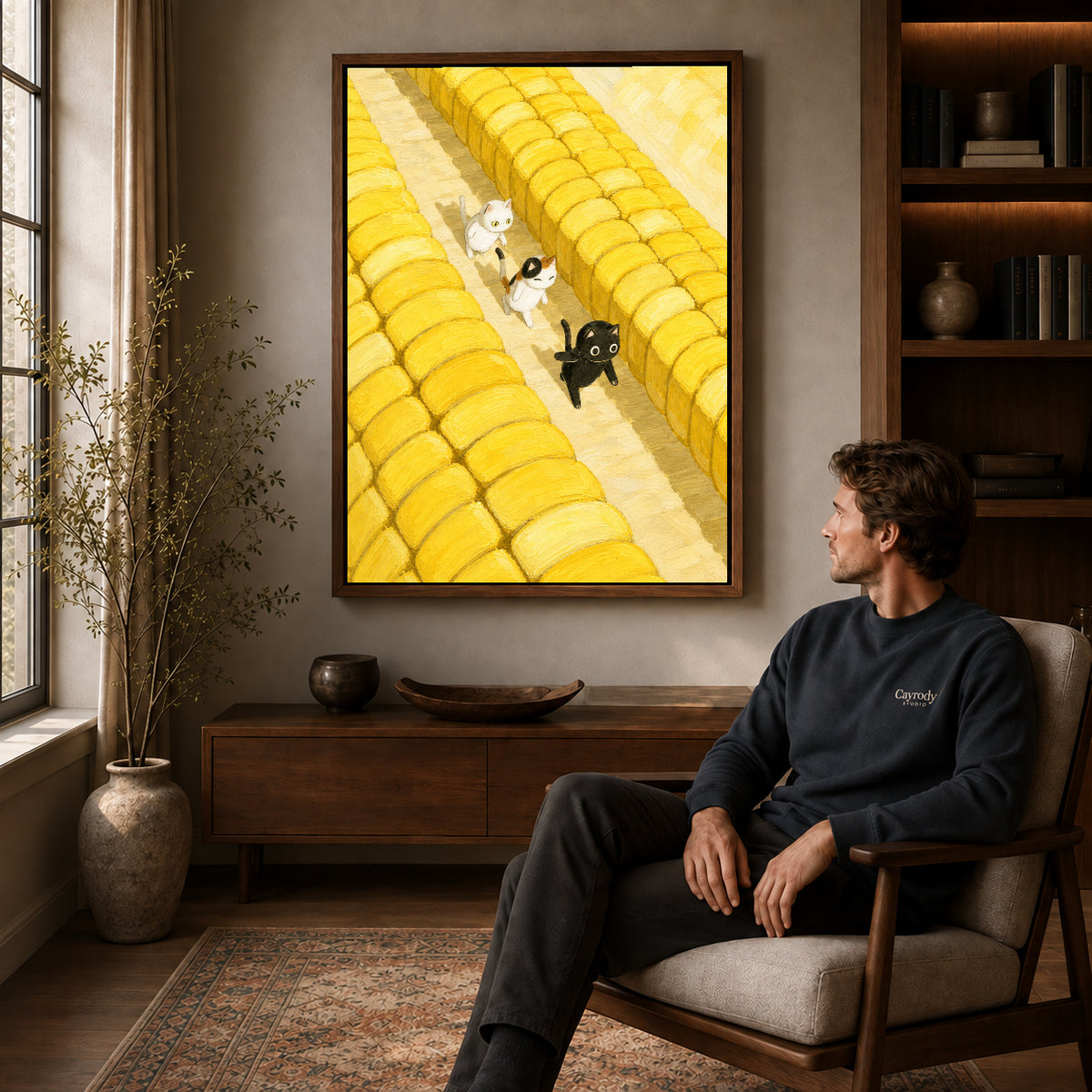Farm cats canvas art in a walnut frame above a console beside a seated man.