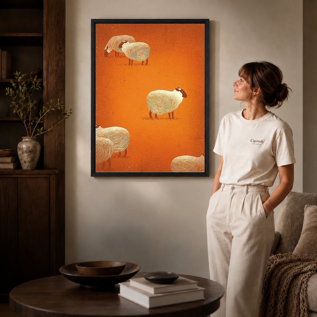 Sheep pattern canvas art in a black frame beside a woman and round wooden table.