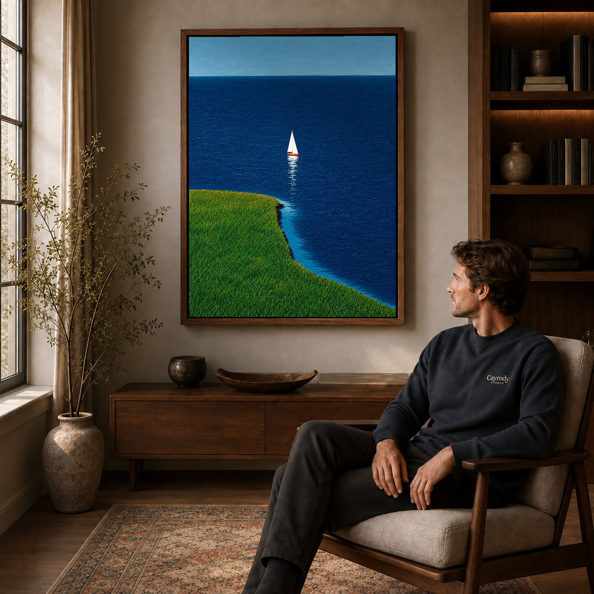 Coastal sailboat canvas art in a walnut frame above a console beside a seated man.