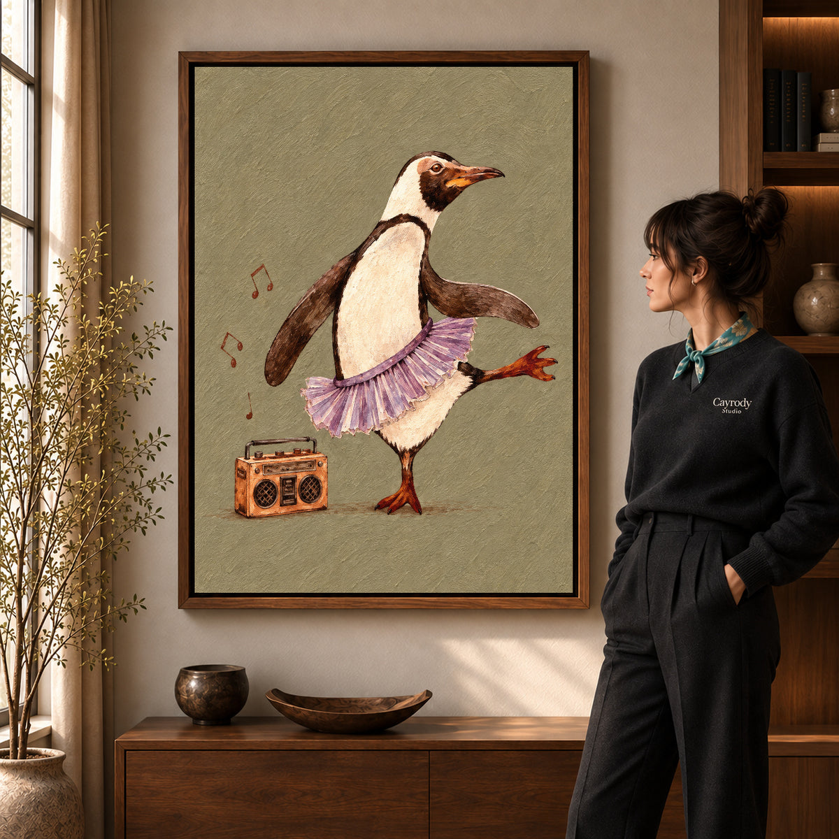 Dancing penguin canvas art in a walnut frame beside a standing woman and wooden console.