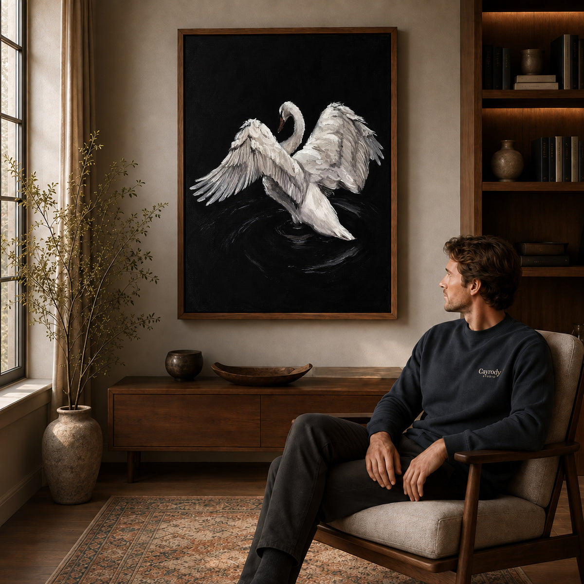 White swan canvas art in a walnut frame above a console beside a seated man.