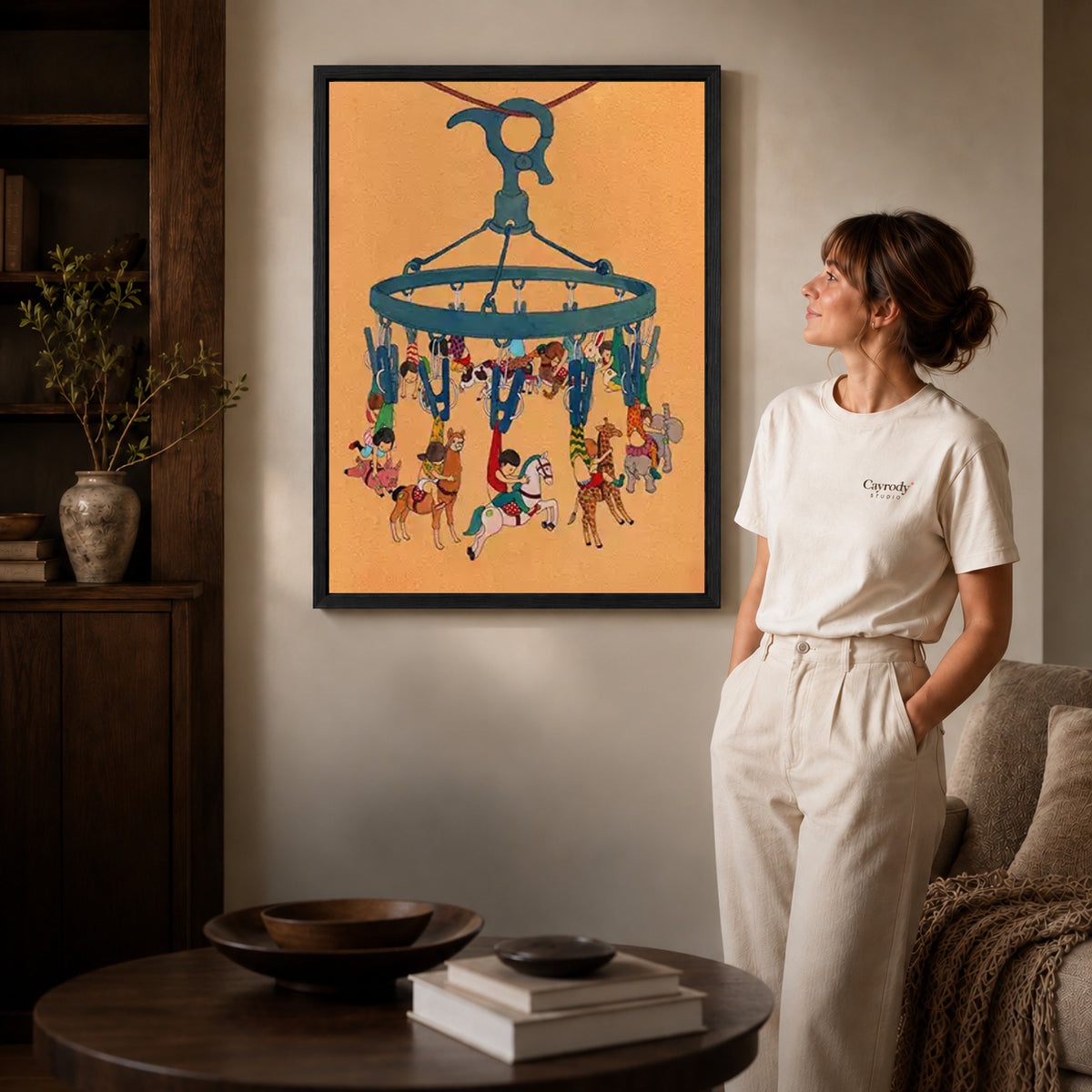 Hanging carousel canvas art in a black frame beside a woman and round wooden table.