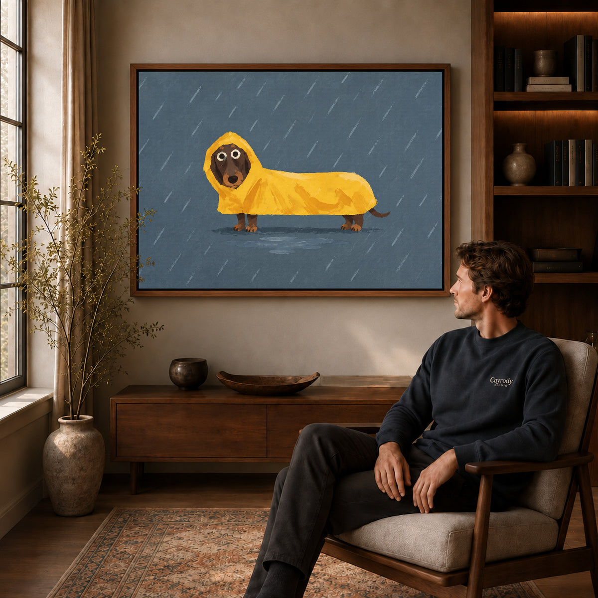 Dachshund raincoat canvas art in a walnut frame above a console beside a seated man.