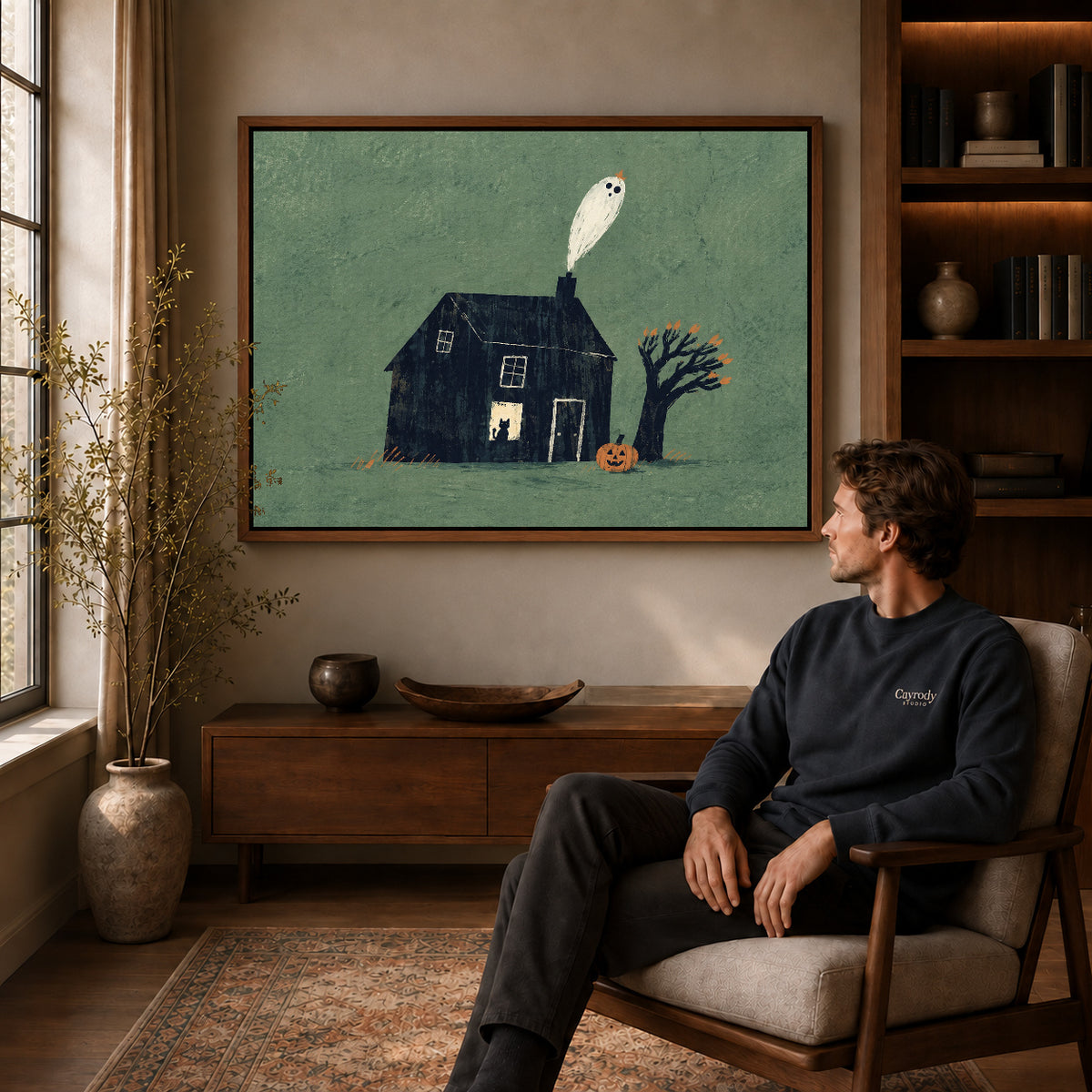 Ghost house canvas art in a walnut frame above a console beside a seated man.