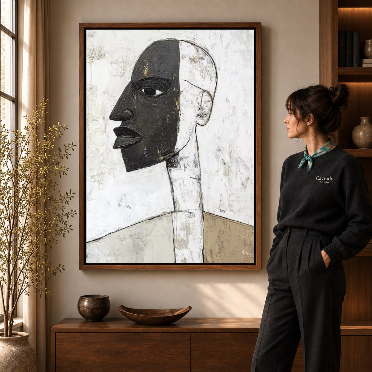 Abstract profile canvas art in a walnut frame beside a standing woman and wooden console.