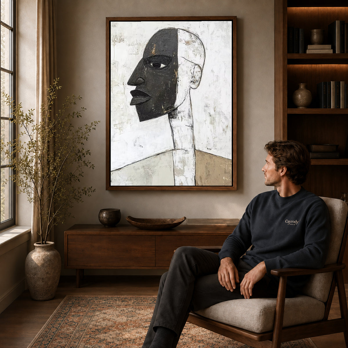 Abstract profile canvas art in a walnut frame above a console beside a seated man.